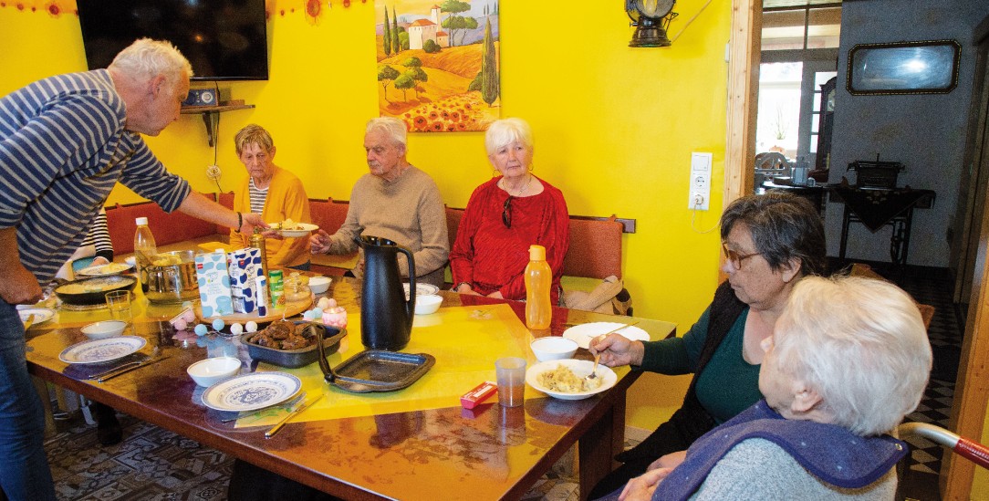 Familiär und ein bisschen rustikal: Gemeinsames Mittagessen in der farbenfrohen Küche der Senioren-WG. Altenpfleger Heinrich Ekenhorst reicht den Teller an, Carolina Springer unterstützt eine Bewohnerin beim Essen. (Foto: Karin Desmarowitz)