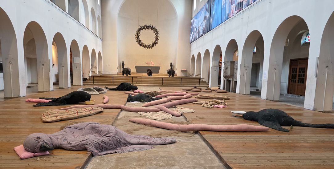 Zuflucht für erschöpfte Wesen: »When Animals Fall from the Sky« von Eva Kotátková in der Christ-König-Kirche in Bochum. Die Werke von Małgorzata Mirga-Tas im Hintergrund bewahren die Erinnerung an Roma-Geschichte. (Foto: Anne Strotmann)
