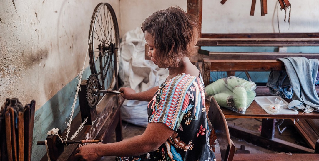 Vor dem Weben spinnt »Mama Prisca« das Garn. Das Spinnrad ist aus einer Fahrradfelge gebaut. Per Hand treibt sie es mit einer Fahrradkette an. (Foto: Manuela Federl)