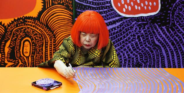 Yayoi Kusama arbeitet an der Werkreihe »My Eternal Soul« (2009–2021). Sie malt sitzend an einer über den Tisch gespannten Leinwand, von unterschiedlichen Seiten, bis die Fläche von einem Geflecht organischer Formen überzogen ist. Es gibt keine Vorgabe, kein Oben und Unten, keine Hierarchie. (Foto: ©Yayoi Kusama/Coutesy of Ota Fine Arts/David Zwirner)